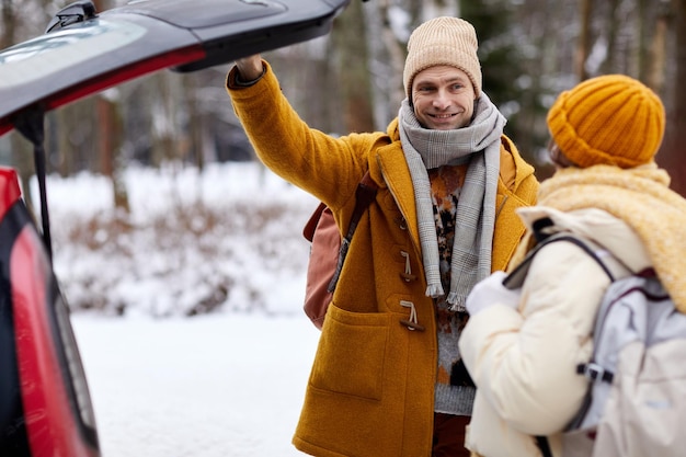 Retrato de um jovem casal sorridente abrindo o porta-malas do carro no inverno enquanto viaja para férias copiam o espaço