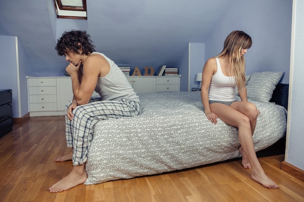 Retrato de um jovem casal zangado, sentado na cama, de costas um para o outro, depois de uma dura briga. Conceito de relacionamento e problemas de casal.
