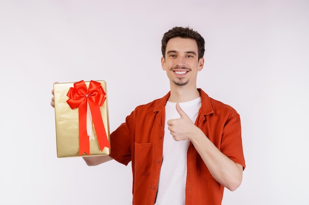 Retrato de um jovem caucasiano feliz mostrando a caixa de presente e olhando para a câmera isolada sobre fundo branco