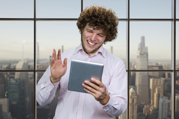 Foto retrato de um jovem caucasiano feliz segurando o dispositivo tablet e acenando com a mão