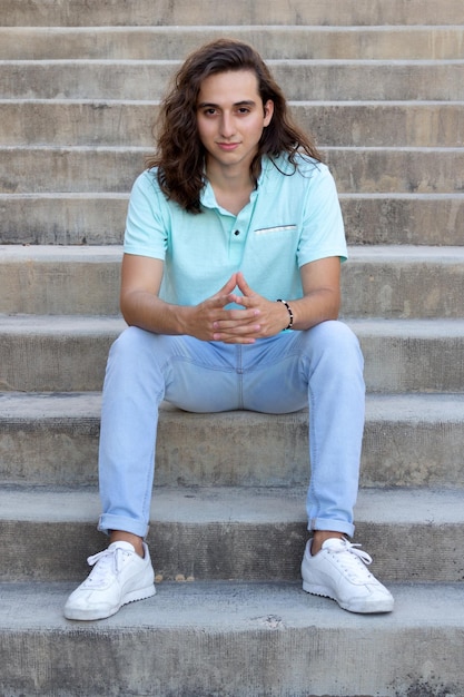 retrato de um jovem com cabelo comprido sentado na escada olhando para a câmera