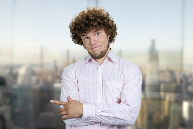 Foto retrato de um jovem com cabelos encaracolados apontando para a esquerda com o dedo indicador borrada paisagem urbana