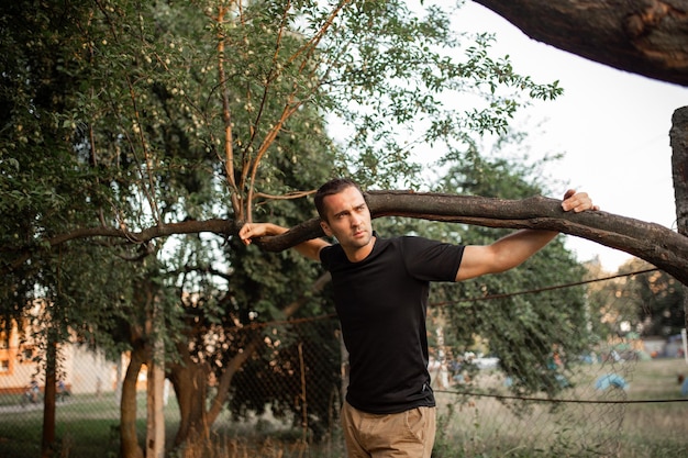 Retrato de um jovem com cerdas leves em uma camiseta preta segurando um galho de árvore