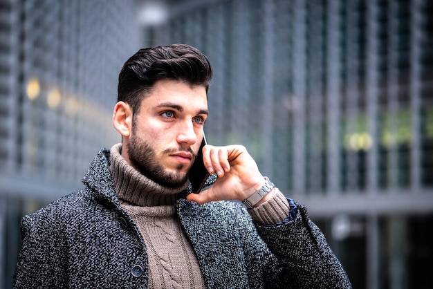 Retrato de um jovem com intenso empresário moderno usando smartphone para trabalhar modelo masculino com olhos azuis, cabelo escuro e barba curta, expressão confiante e séria