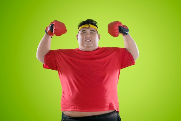 Retrato de um jovem com sobrepeso flexionando os músculos enquanto está de pé contra um fundo colorido