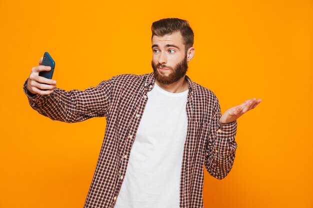 Retrato de um jovem confuso, vestindo roupas casuais, tirando uma selfie
