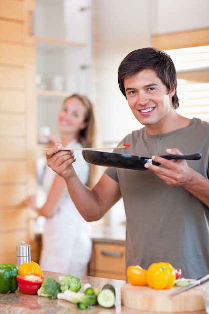 Retrato de um jovem cozinhar enquanto sua esposa está lavando o di