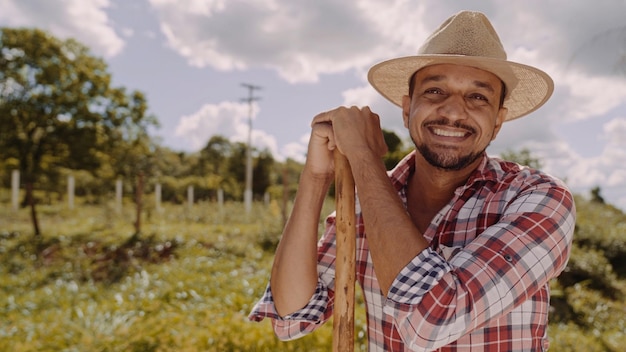 Retrato de um jovem de camisa casual segurando sua enxada na fazenda Ferramenta agrícola Homem latino