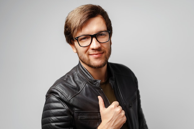 Retrato de um jovem de óculos, vestindo uma jaqueta de couro preta com fundo cinza