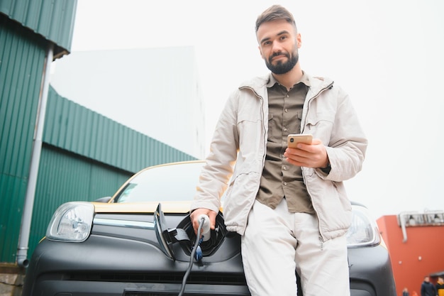 Retrato de um jovem de pé com cabo de carregamento perto da estação de carregamento