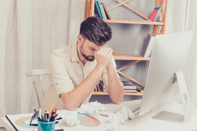 Retrato de um jovem deprimido e cansado sentado à mesa