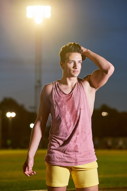 Retrato de um jovem desportista suor muscular posando no estádio