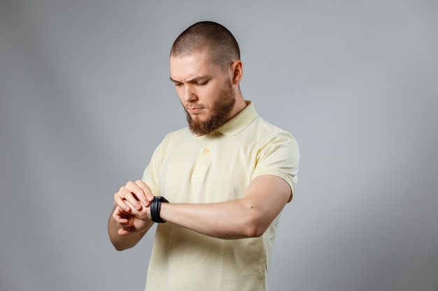 Retrato de um jovem em uma camiseta amarela olha para o relógio em cinza.