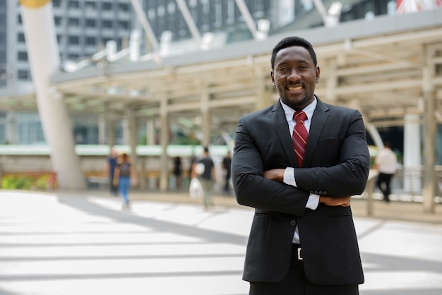 Retrato de um jovem empresário africano bonito em um terno contra a vista de um edifício moderno ao ar livre na cidade