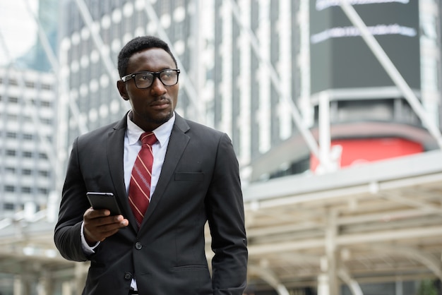 Retrato de um jovem empresário africano bonito em um terno contra a vista de um edifício moderno ao ar livre na cidade