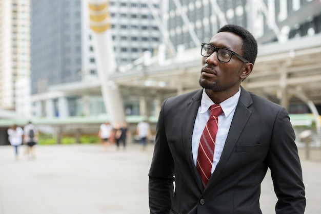 Retrato de um jovem empresário africano bonito em um terno contra a vista de um edifício moderno ao ar livre na cidade