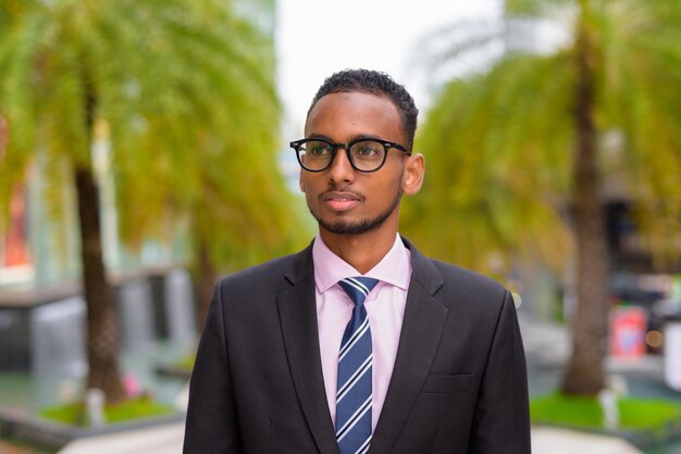 Retrato de um jovem empresário africano bonito pensando ao ar livre na cidade