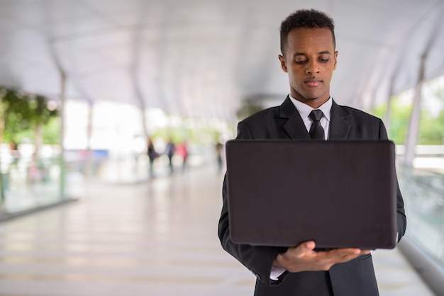 Retrato de um jovem empresário africano de sucesso ao ar livre usando um laptop