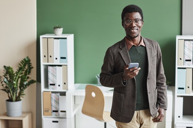 Retrato de um jovem empresário africano em roupas casuais, sorrindo enquanto usa seu telefone celular no escritório