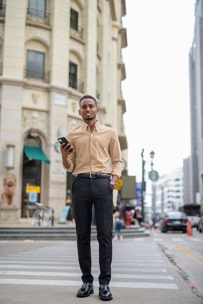 Retrato de um jovem empresário africano negro vestindo roupas casuais ao ar livre na cidade e usando telefone celular