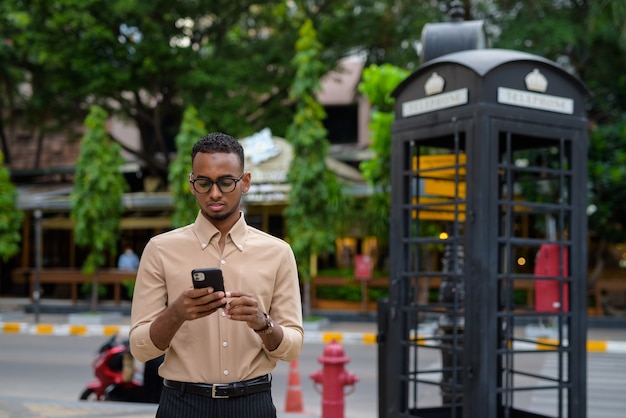 Retrato de um jovem empresário africano negro vestindo roupas casuais ao ar livre na cidade e usando telefone celular