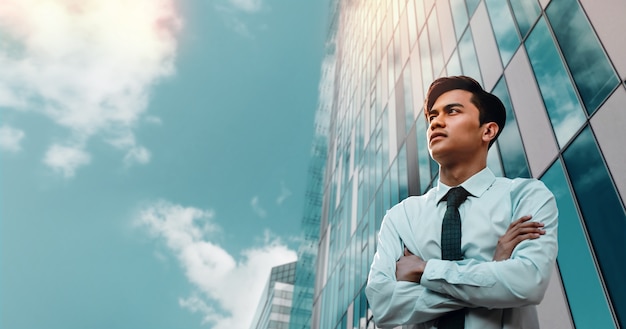 Retrato de um jovem empresário asiático na cidade. braços cruzados e olhando para o céu.
