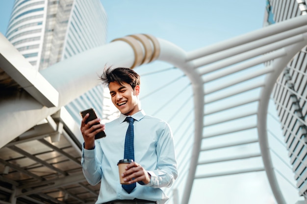 Retrato de um jovem empresário asiático sorridente usando telefone celular na cidade