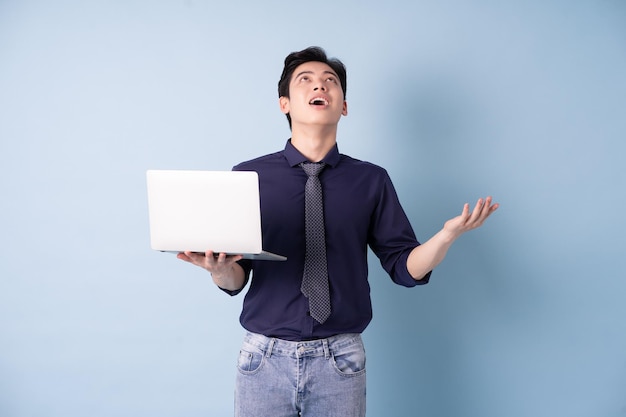 Retrato de um jovem empresário asiático usando laptop em fundo azul