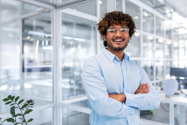 Retrato de um jovem empresário de programador designer indiano de pé no escritório usando óculos