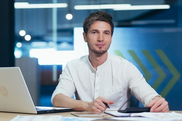 Retrato de um jovem empresário em roupas modernas, trabalhando com documentos e olhando seriamente para a câmera