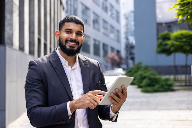 Foto retrato de um jovem empresário indiano de pé na rua perto do escritório e usando um tablet