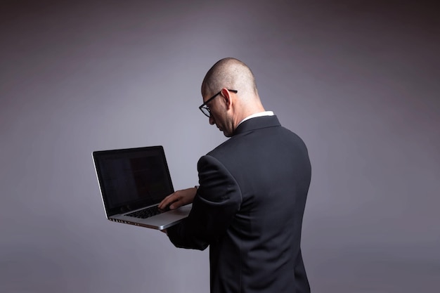 Retrato de um jovem empresário latino de terno em pé segurando e olhando para a tela do computador portátil isolado sobre fundo cinza