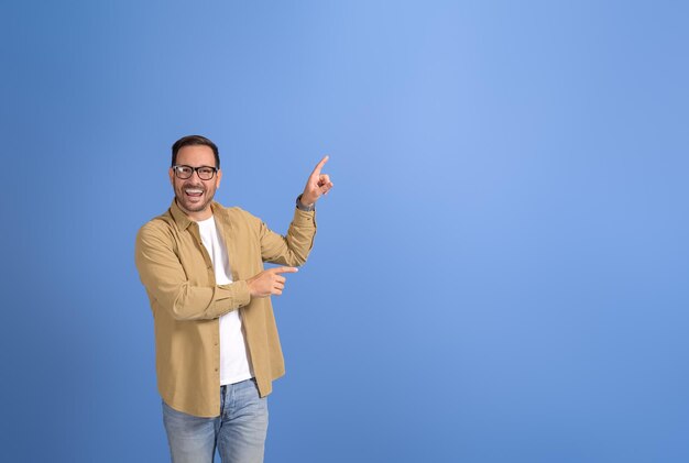 Foto retrato de um jovem empresário rindo e apontando para o espaço de cópia para publicidade em fundo azul