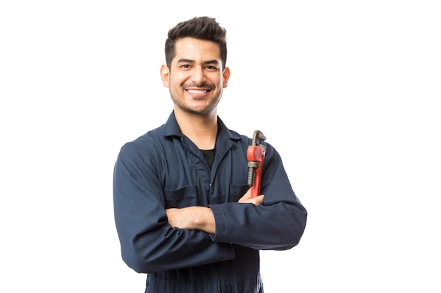 Foto retrato de um jovem encanador masculino sorridente com os braços em pé de chave de cano cruzados sobre fundo branco