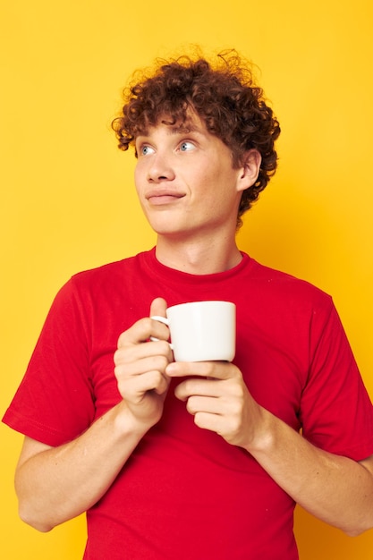 Retrato de um jovem encaracolado em uma camiseta vermelha com um boné branco nas mãos isolado de fundo inalterado