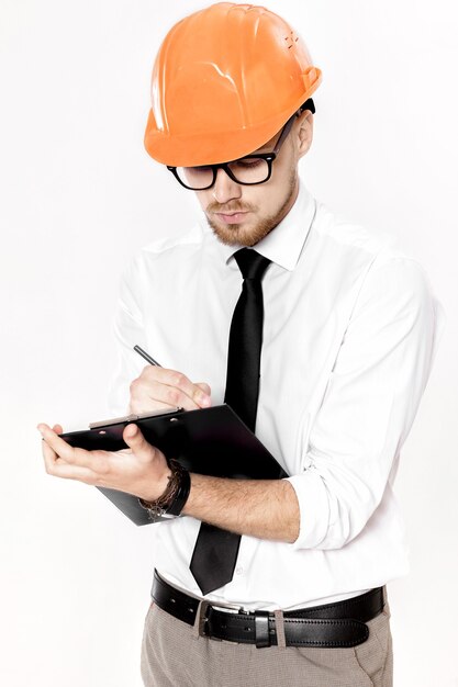 Retrato de um jovem engenheiro civil em um capacete laranja com uma pasta em um fundo branco