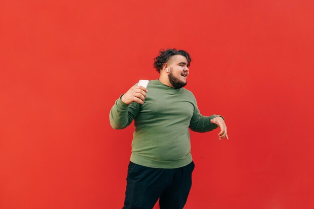 Retrato de um jovem engraçado com excesso de peso de pé sobre um fundo vermelho com um smartphone na mão