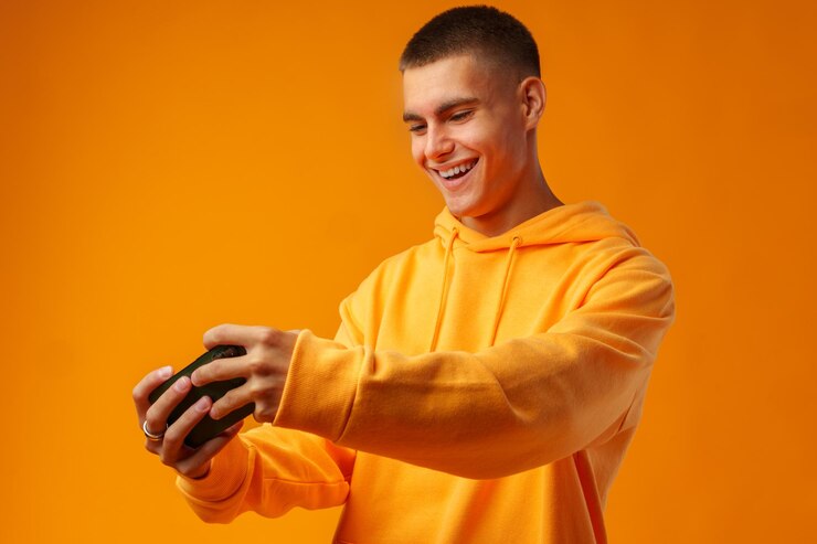 Foto retrato de um jovem entusiasmado jogando um jogo on-line em um telefone móvel em fundo amarelo