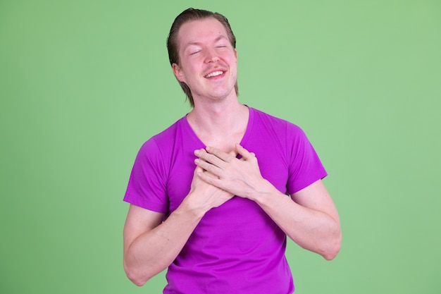 Retrato de um jovem escandinavo bonito vestindo uma camisa roxa contra o chroma key ou uma parede verde