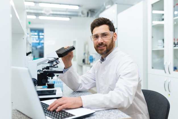 Retrato de um jovem estudante do sexo masculino, um estagiário sentado em uma mesa de laboratório estudando em um laptop e