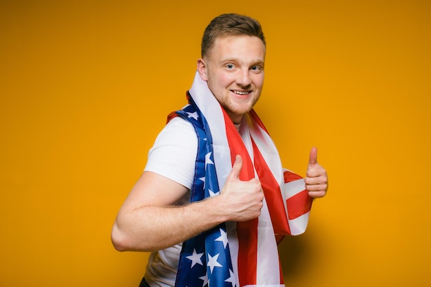 Retrato de um jovem feliz com barba em roupas casuais, segurando a bandeira dos eua