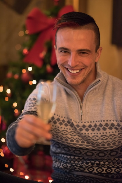 Retrato de um jovem feliz com uma taça de champanhe comemorando as férias de inverno em casa lindamente decorada para o natal