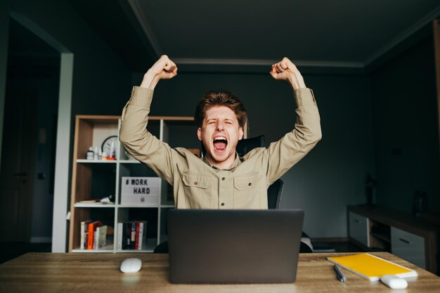 Retrato de um jovem feliz em um trabalho à distância se alegra com o sucesso do projeto concluído Freelancer