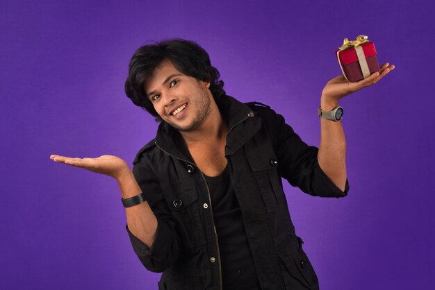 Retrato de um jovem feliz sorridente e bonito segurando a caixa de presente em um fundo roxo