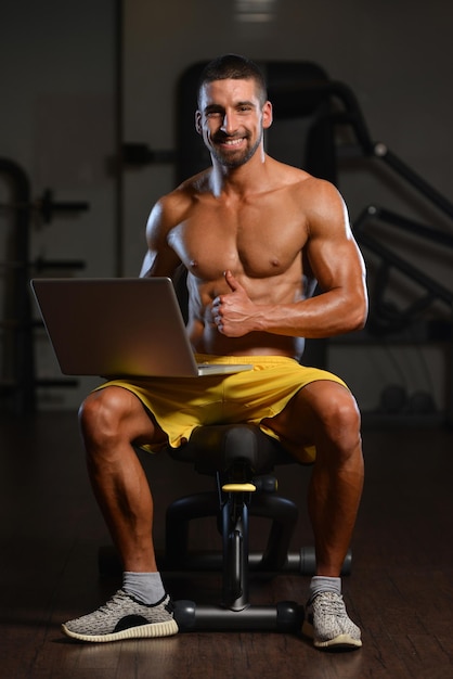 Retrato de um jovem fisicamente apto usando laptop musculoso fisiculturista fitness modelo uso computador