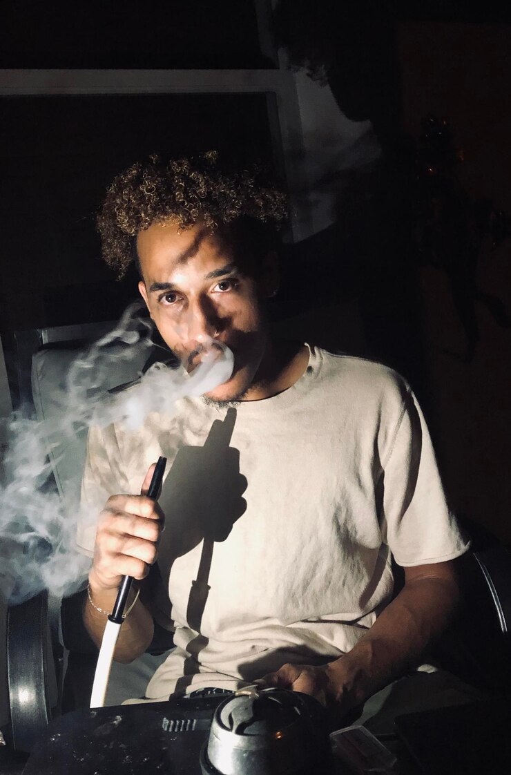 Foto retrato de um jovem fumando narguilé em casa