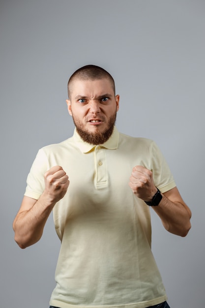 Retrato de um jovem homem bravo em uma camiseta amarela com os punhos no cinza ..