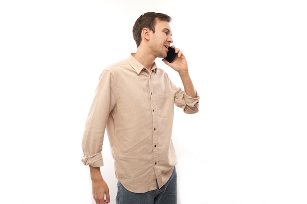 Retrato de um jovem homem caucasiano bonito sorrindo e falando no celular isolado no fundo branco do estúdio