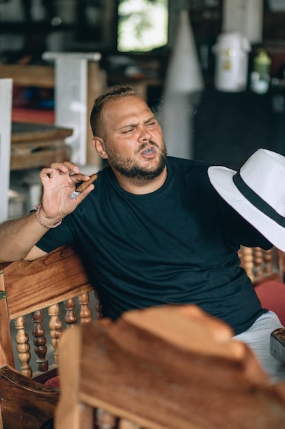 Retrato de um jovem imponentemente estendido em um sofá, fumando um charuto e curtindo o clima de verão. Conceito de férias.