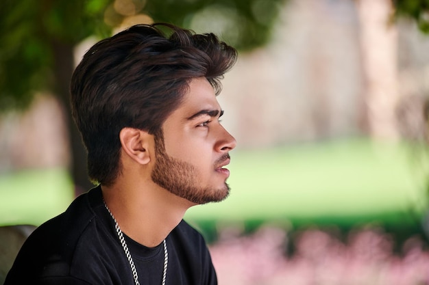 Retrato de um jovem indiano atraente em camiseta preta e corrente de pescoço prateada no fundo do parque verde